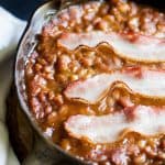 a skillet of baked beans with bacon slices on top
