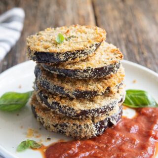a stack of baked eggplant slices on a plate with marinara sauce and basil