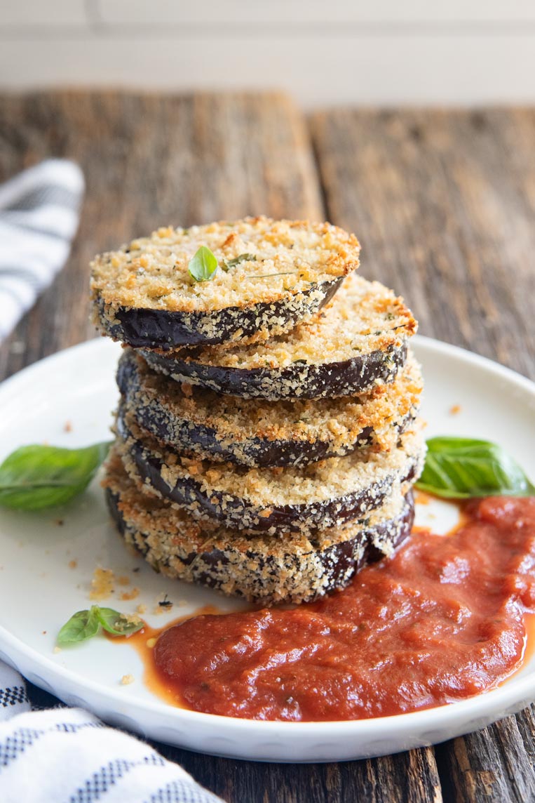a stack of baked eggplant slices on a plate with marinara sauce and basil
