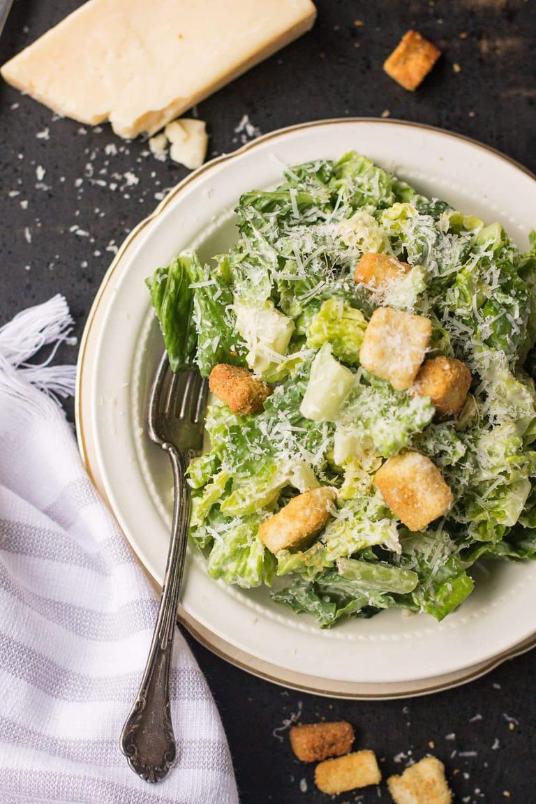 a bowl of caesar salad with a fork in it and parmesan cheese on the side
