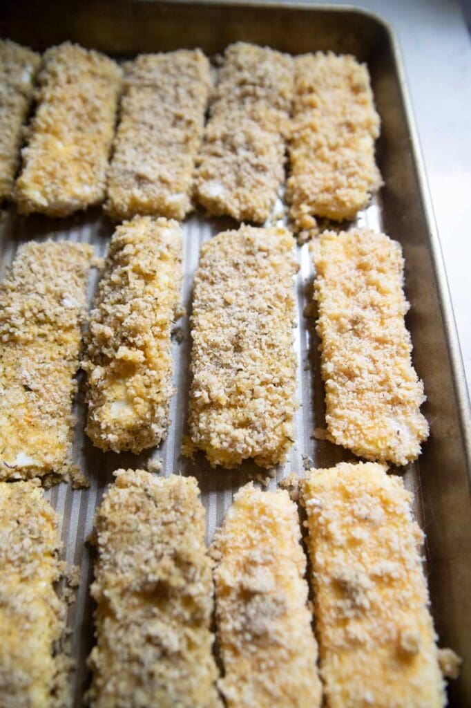 a cookie sheet with breaded cheese sticks ready for the freezer 