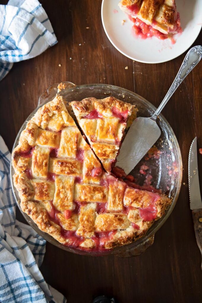 a tart cherry pie on a table with a slice missing, one slice cut and a pie server