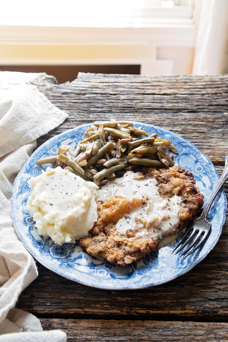 a plate of chicken fried steak with mashed potatoes and green beans on a table 