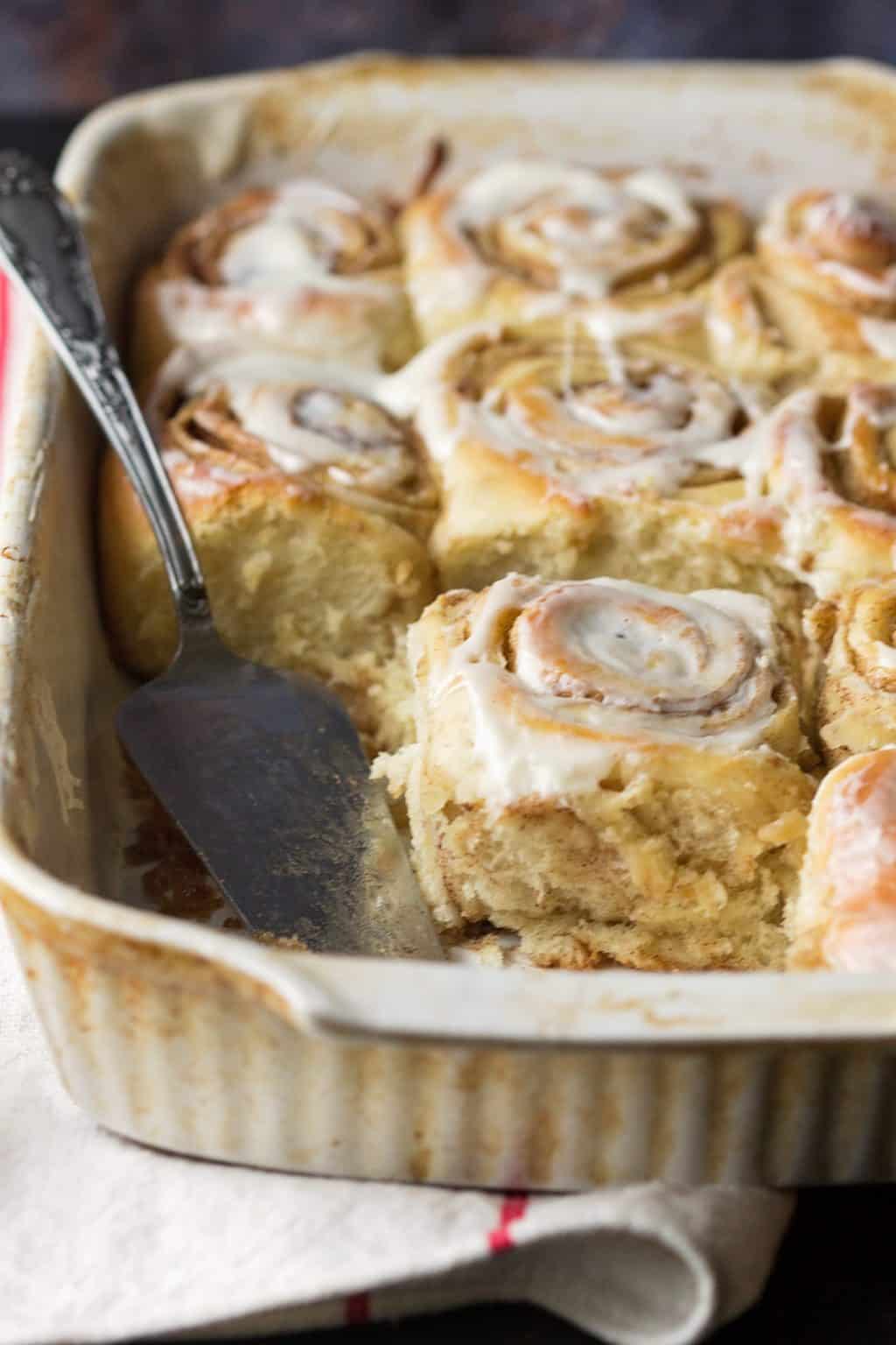 A baking dish of cinnamon rolls with one removed and a spatula inside 