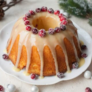 a bundt cake with glaze and cranberries on a white table with christmas decor