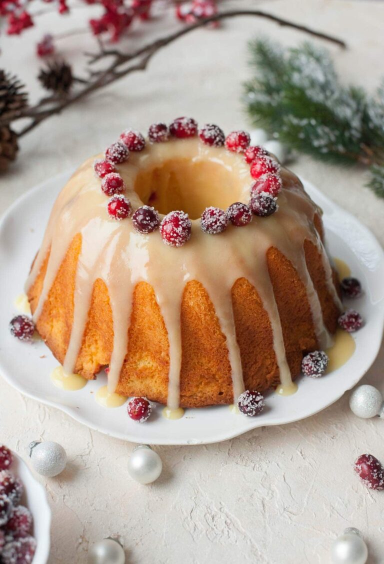 a bundt cake with glaze and cranberries on a white table with christmas decor