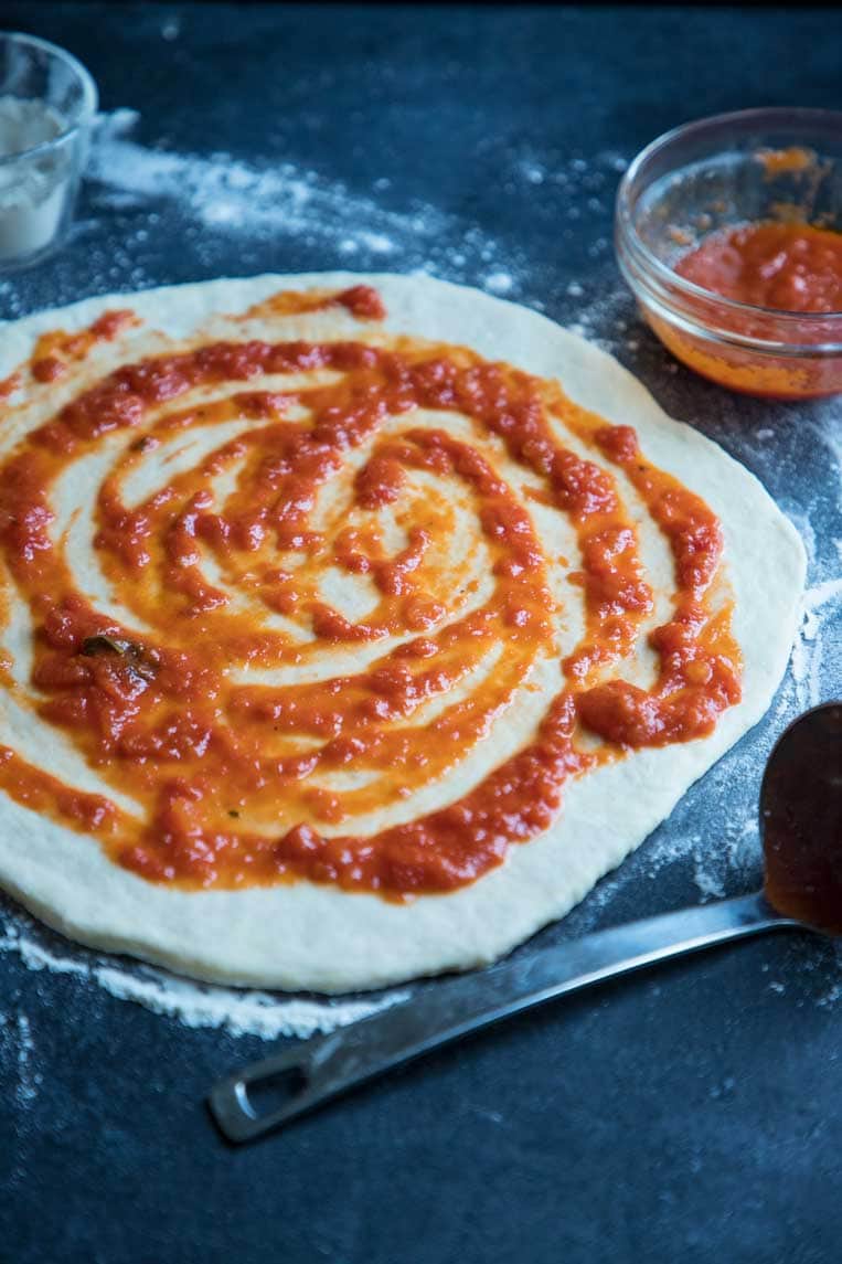 pizza dough on a counter top with pizza sauce