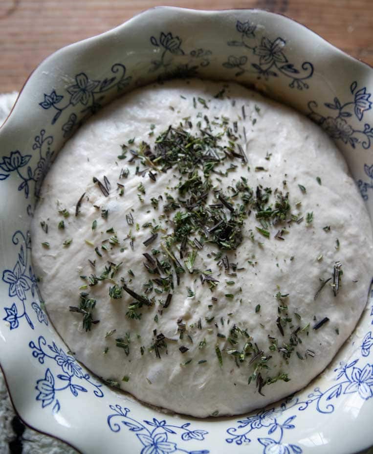a bowl of dough with herbs sprinkled on top to be mixed in 