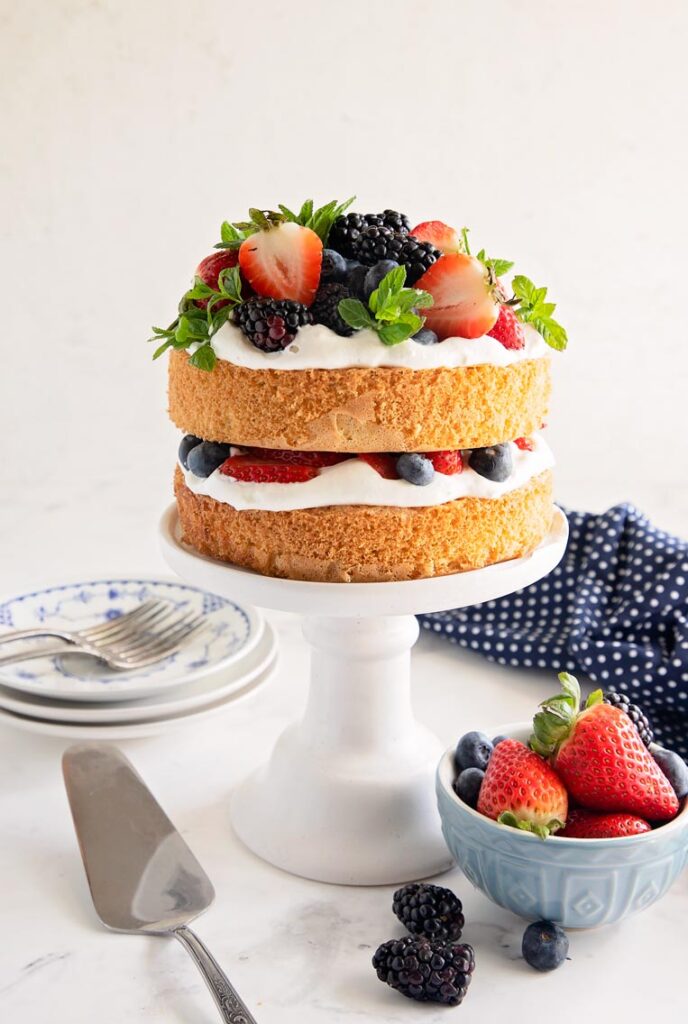 a stacked genoise sponge cake on a stand with cream between the layers and berries on top