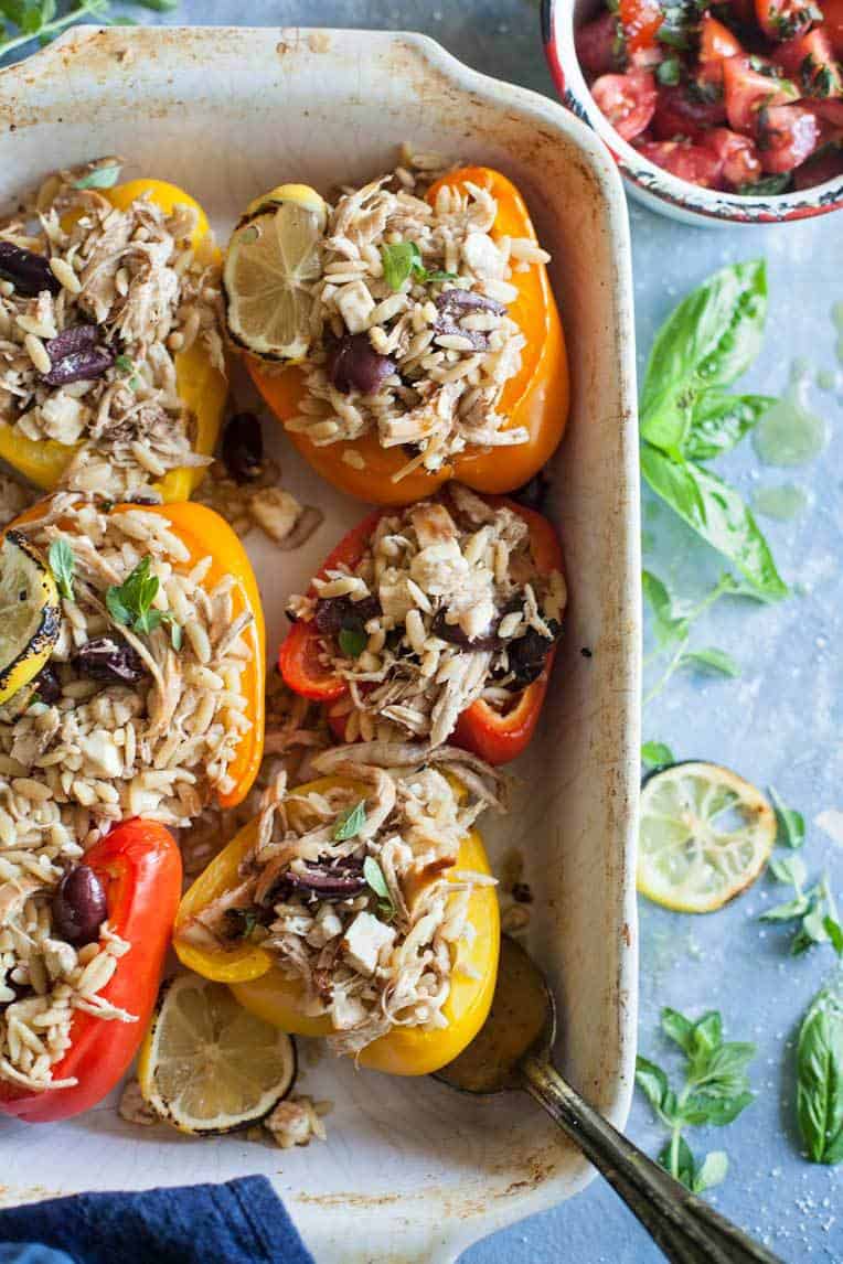 Greek stuffed peppers in a white dish with basil.
