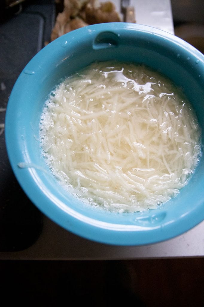 a bowl of hash browns in cold water to rinse away starch 