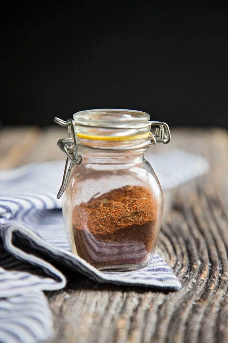a glass jar of taco seasoning on a table with a blue striped napkin
