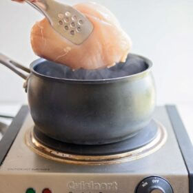 a pot of boiling water with a chicken breast being placed inside