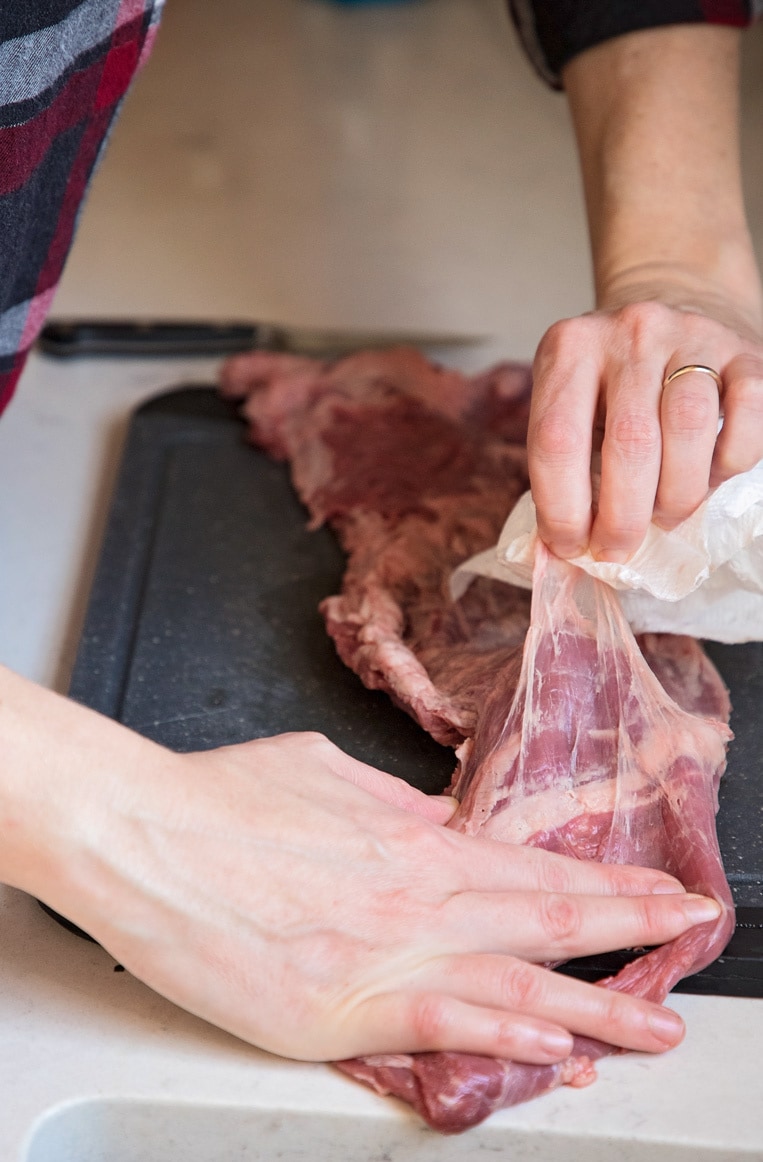 a person using a napkin to grab and pull away the connective tissue from the back of a skirt steak 