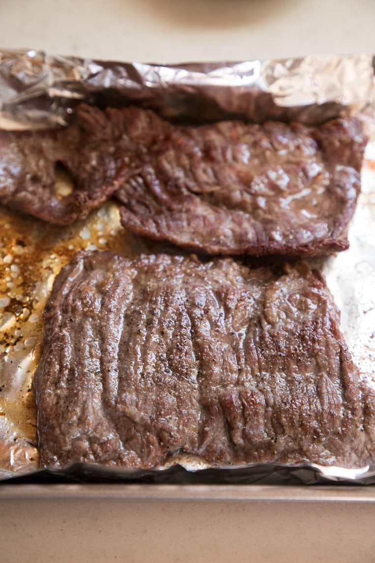 a broiled skirt steak resting on its baking sheet before cutting 