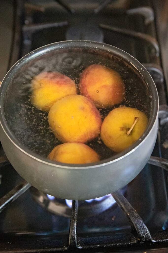 a pot of boiling water with 5 peaches inside. 