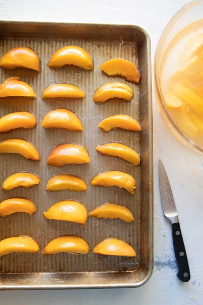 a cookie sheet with peach slices  laid out to freeze 