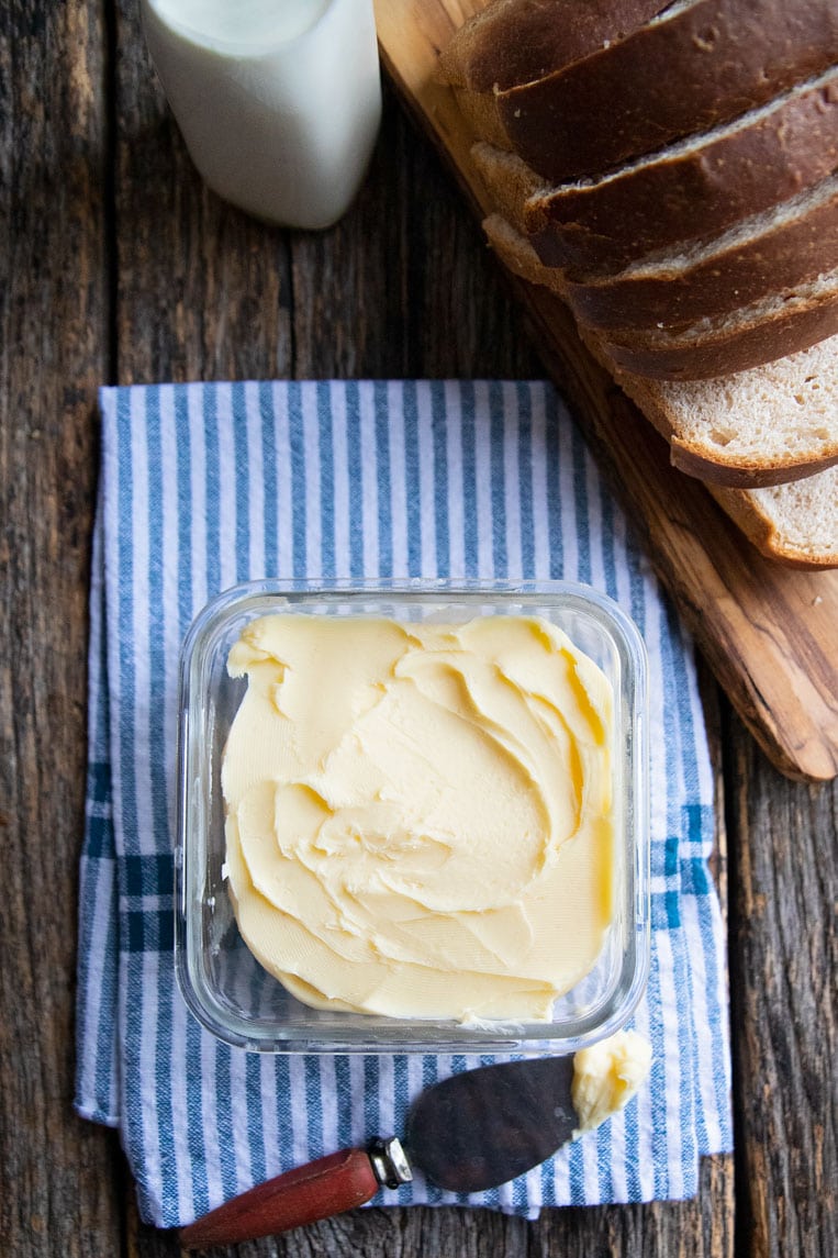 a container of butter on a table with bread