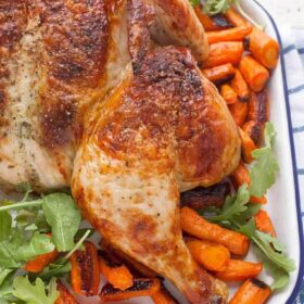 A roast chicken on a tray with carrots