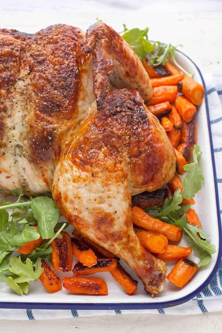 A roast chicken on a tray with carrots
