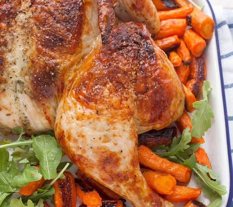 a roast chicken on a pan with carrots