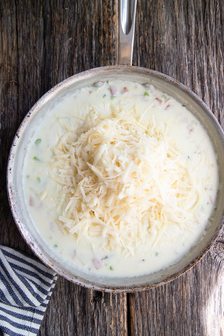 a skillet of cream sauce with a pile of cheese on top 
