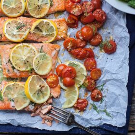 baked salmon filet on a sheet pan with tomatoes and lemons
