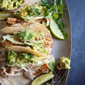 Easy grilled fish tacos piled together on a plate with chunky avocado cream