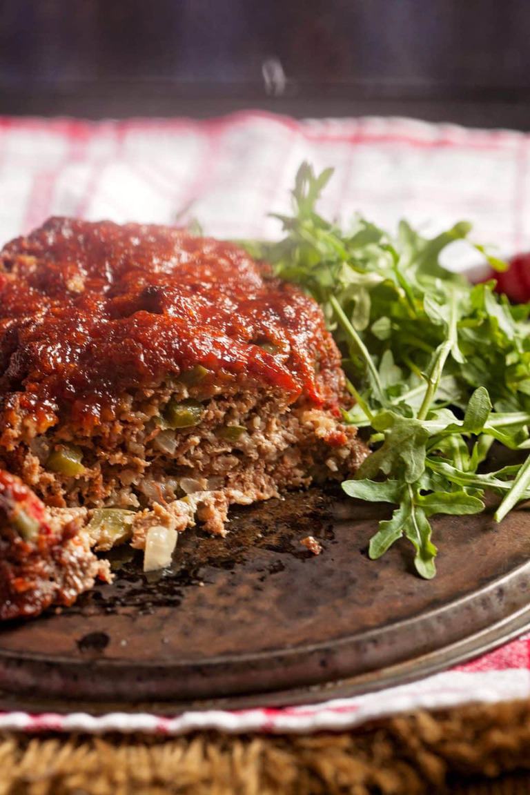 sliced meatloaf with red sauce on a brown plate with a green salad on a red and white and white napkin