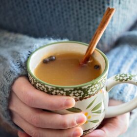 holding a mug of mulled cider with a cinnamon stick.