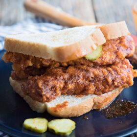 A sandwich of hot fried chicken with pickles on a plate