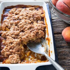 a big pan of fresh peach cobbler with a spoon in it by a window