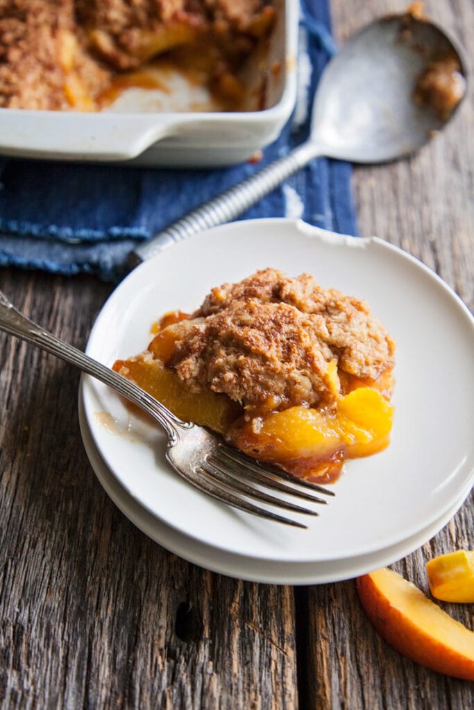 Fresh peach cobbler scooped out onto a plate with a fork.