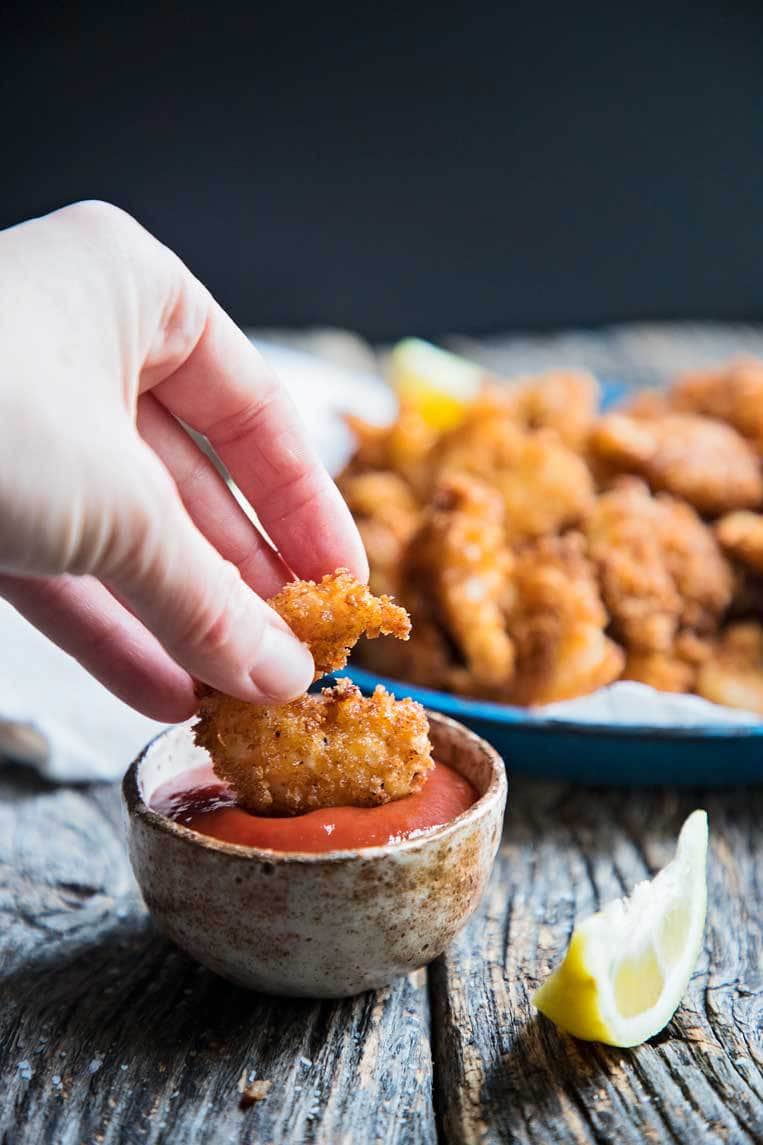 a popcorn shrimp being dipped in a bowl of cocktail sauce