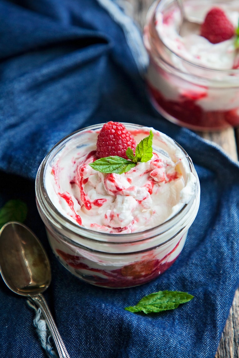 A small jar of raspberry fool in a table with a raspberry on top.