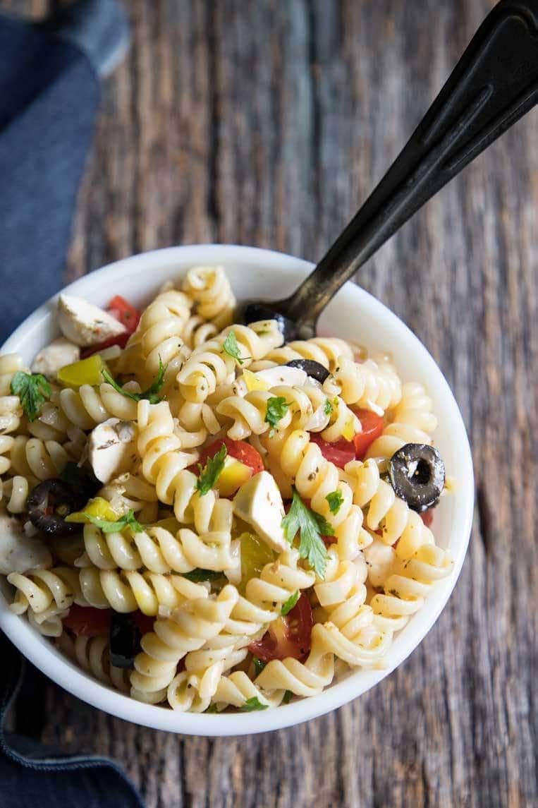 rotini pasta salad with mozzarella and tomato in a bowl with a spoon