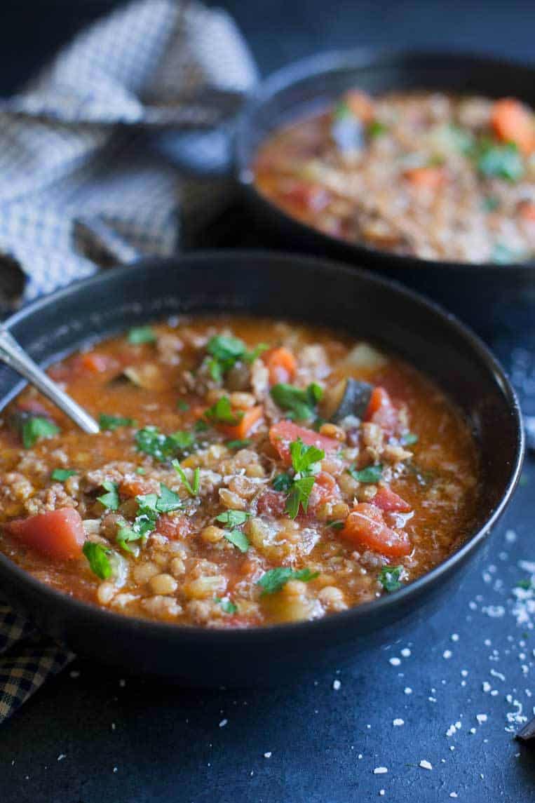 sausage and lentil soup in two bowls with a spoon