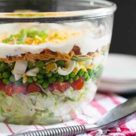 Seven layer salad in a clear bowl on a plaid napkin.