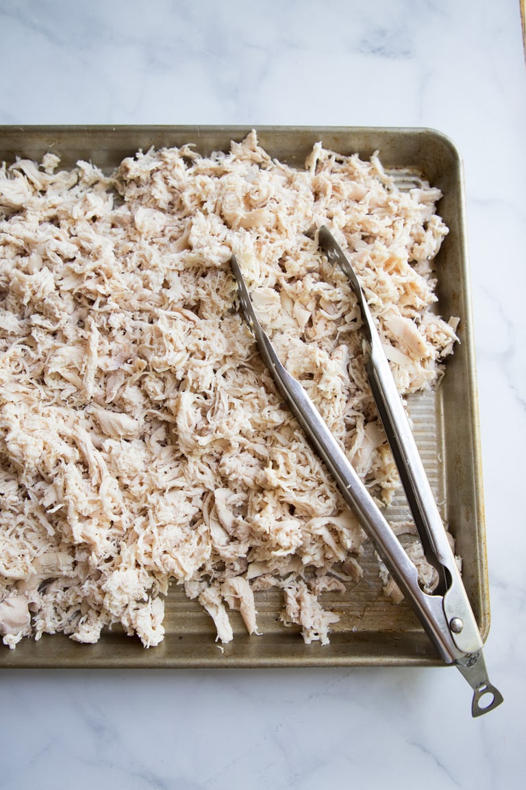 a large cookie sheet of shredded chicken with tongs