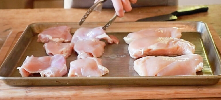 a half sheet pan with chicken thighs and breast meat being prepared to go in the oven 
