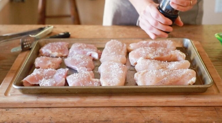 a person sprinkling the chicken with salt and pepper on a baking sheet