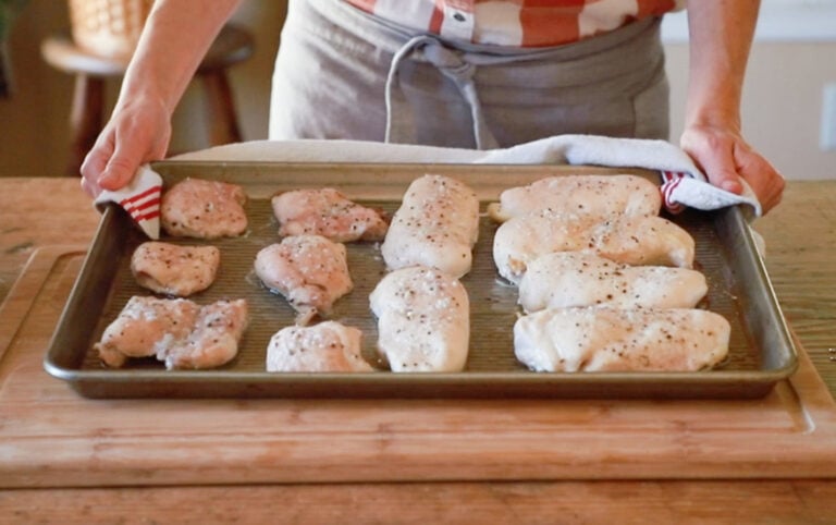 cooked chicken on a cookie sheet being placed on a table by a person