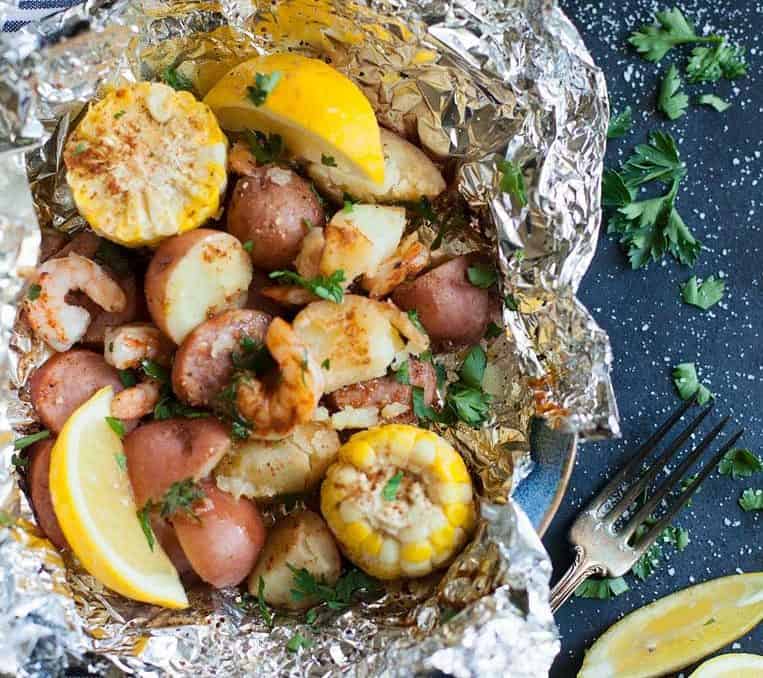  Shrimp, potatoes, corn, and smoked sausage in a foil packet open with a fork 
