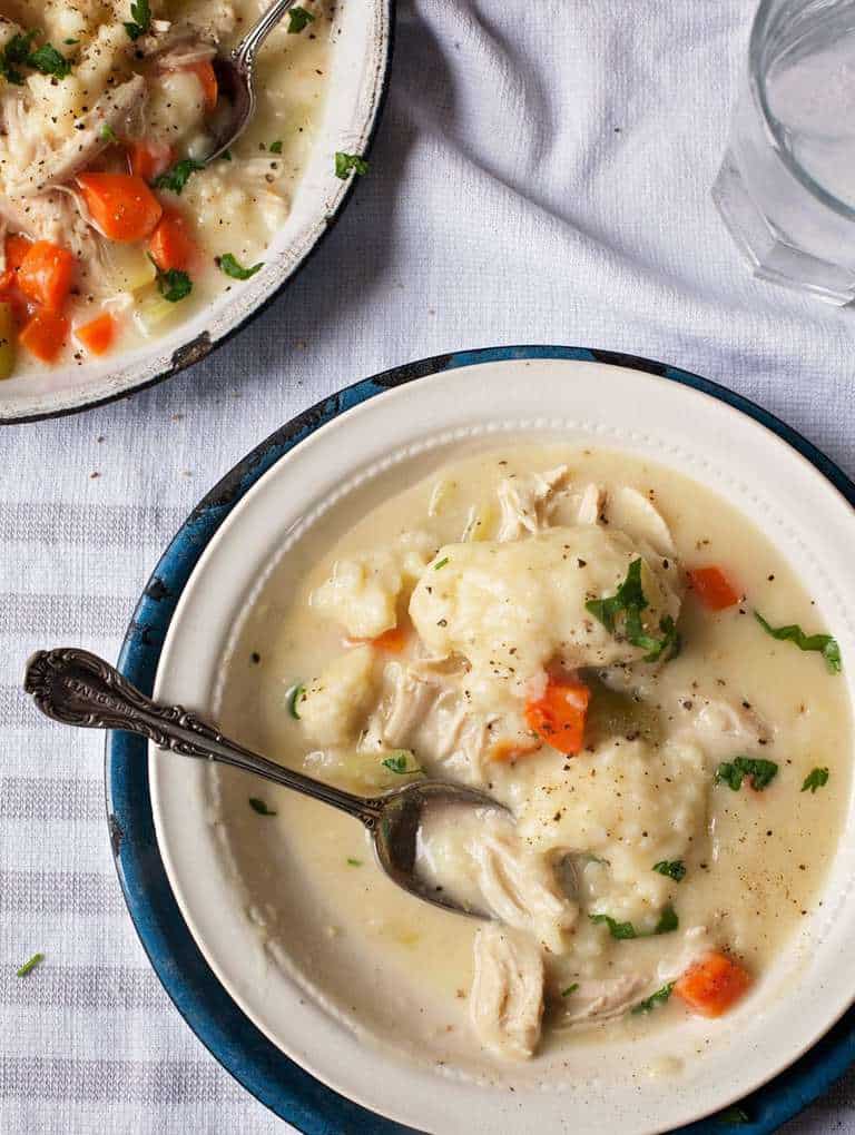 an overhead picture of chicken and dumplings in a white bowl on a table with a spoon 