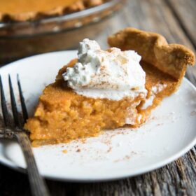 a slice of southern sweet potato pie on a plate with whipped cream and cinnamon