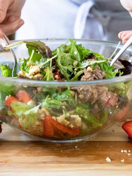 a bowl of steak salad being tossed together with two forks