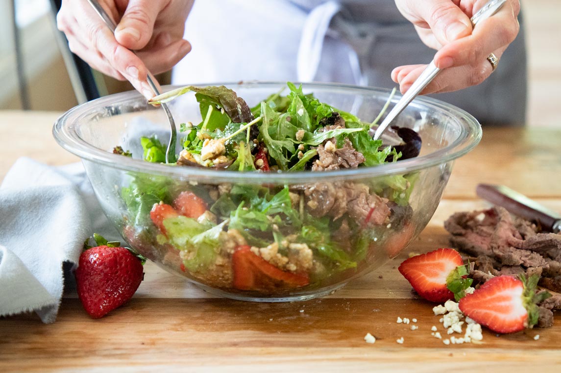 a bowl of steak salad being tossed together with two forks 