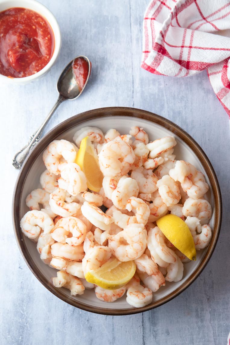 a bowl of steamed shrimp with lemon with cocktail sauce