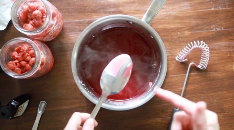 a pot with cherry pie filling after it's been cooked; a spoon showing thickened liquid holds a line