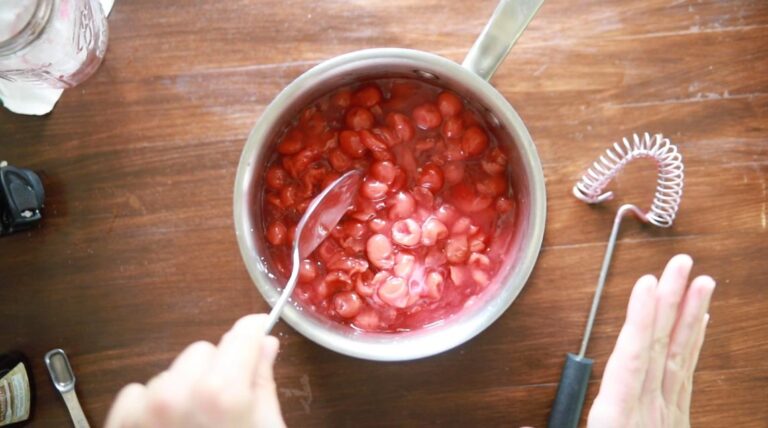 a pot of cherry pie filling with cherries being stirred in 